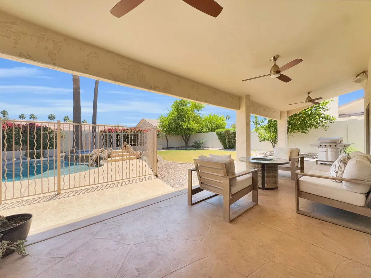 This photo captures a tranquil backyard scene with a well-furnished outdoor seating area, a fenced grassy yard, and the swimming pool. The setting is surrounded by mature greenery, offering privacy and a sense of seclusion. The seating area is ideal for gatherings, reading, or enjoying the Arizona sun.