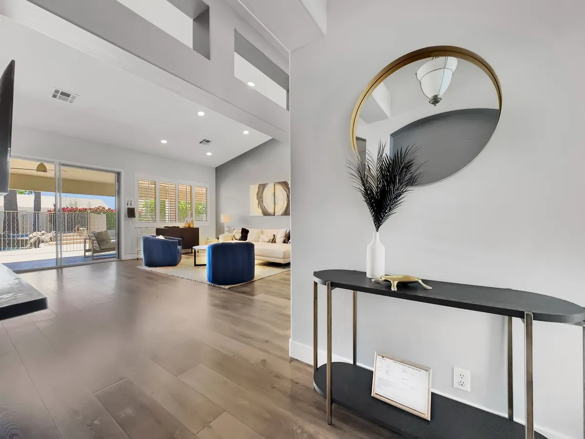 A stylish and inviting living room featuring a large mirror, a modern console table, and a blue accent chair. The space is designed for entertaining guests and socializing, with an open layout that encourages gatherings and relaxation after a day out.