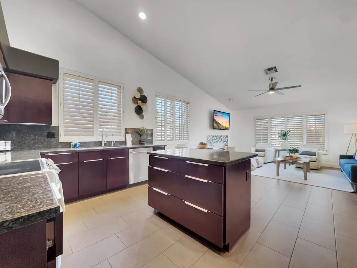 A bright, contemporary kitchen featuring a spacious island, modern stainless steel appliances, and an adjacent cozy living area with a sofa and coffee table. The kitchen is well-equipped, exuding a welcoming atmosphere that hints at gatherings and culinary activity.