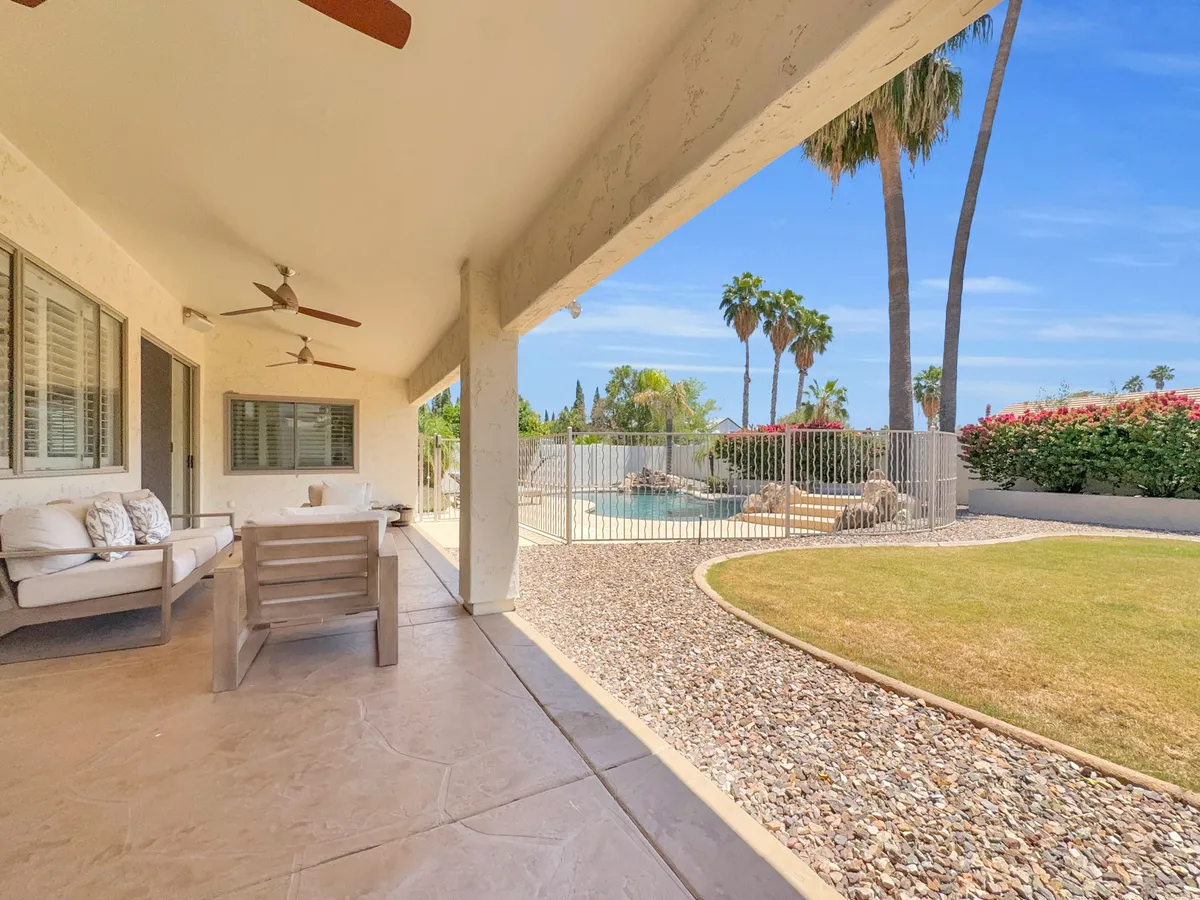 This image captures the inviting backyard featuring a sparkling swimming pool surrounded by patio furniture, palm trees, and flowering bushes. The scene evokes relaxation as well as the opportunity for family fun outdoors, with clear sunset lighting enhancing the welcoming atmosphere.
