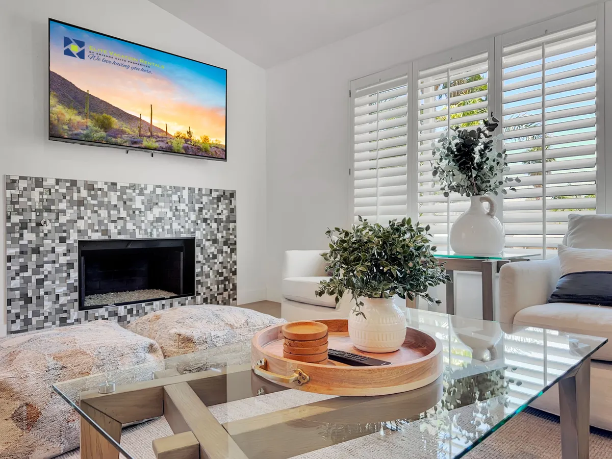 A cozy living area with a contemporary fireplace, TV displaying a sunset, a coffee table decorated with stylish accents, and lush plant arrangements. The space is designed for relaxation and entertaining after a day out.